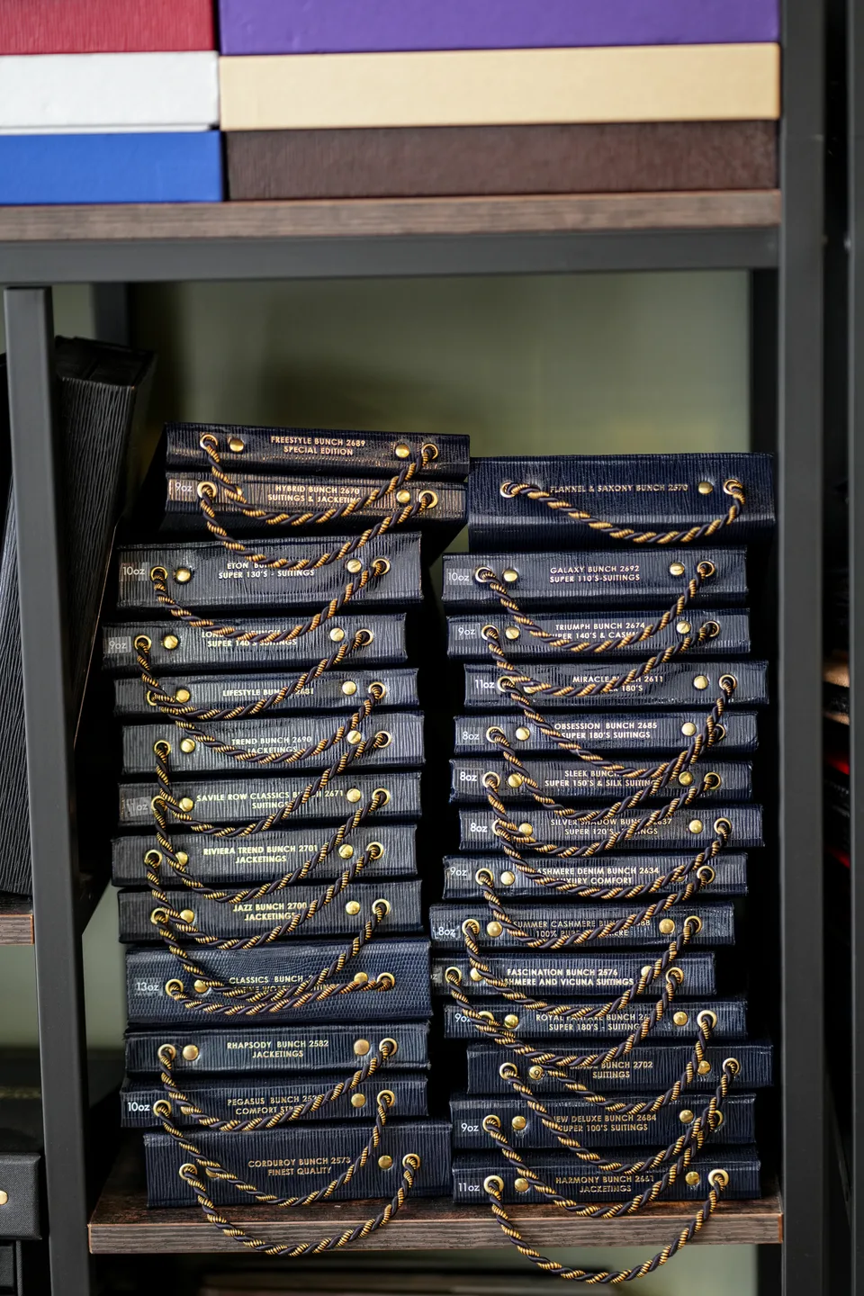 Shelves of cloth bunch books with gilt lettering, from Super 130’s suitings to cashmere