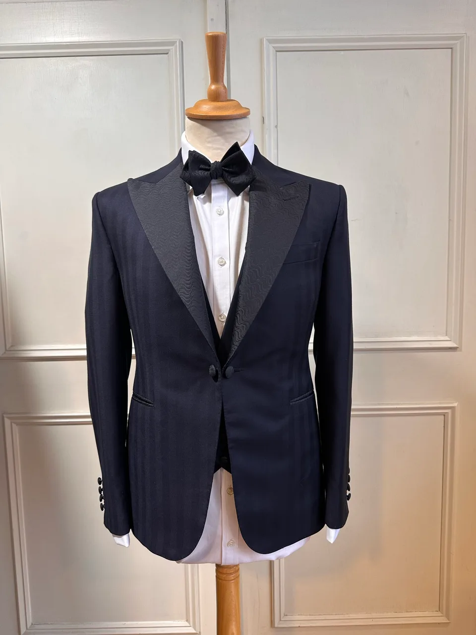Front mannequin view of the midnight jacquard peak-lapel tuxedo, tailored with textured black peak lapels, a one-button front and midnight-blue cloth.