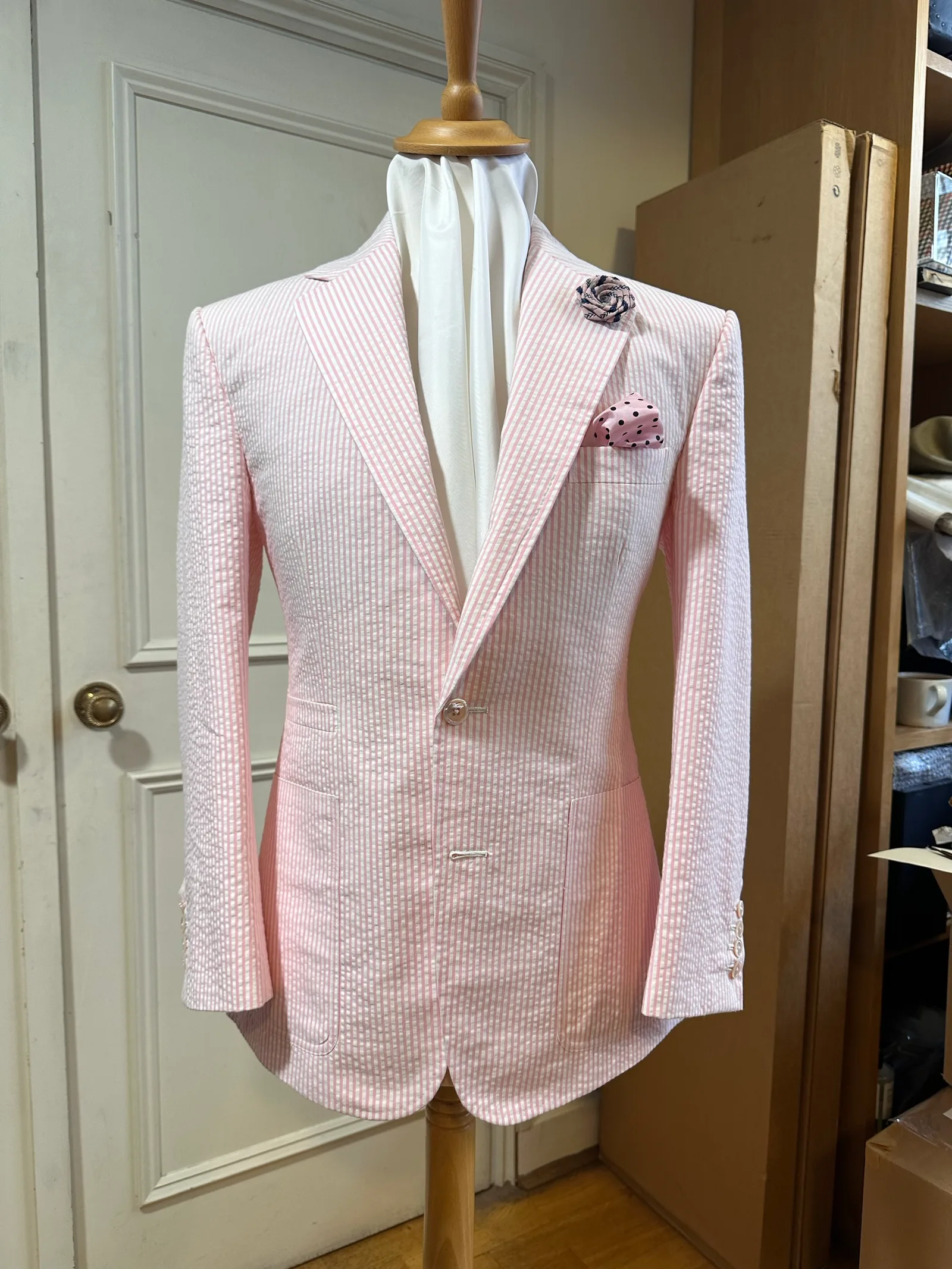 Mannequin view of a pale-pink seersucker jacket, cut with broad peak lapels, a single pale button and rounded fronts.