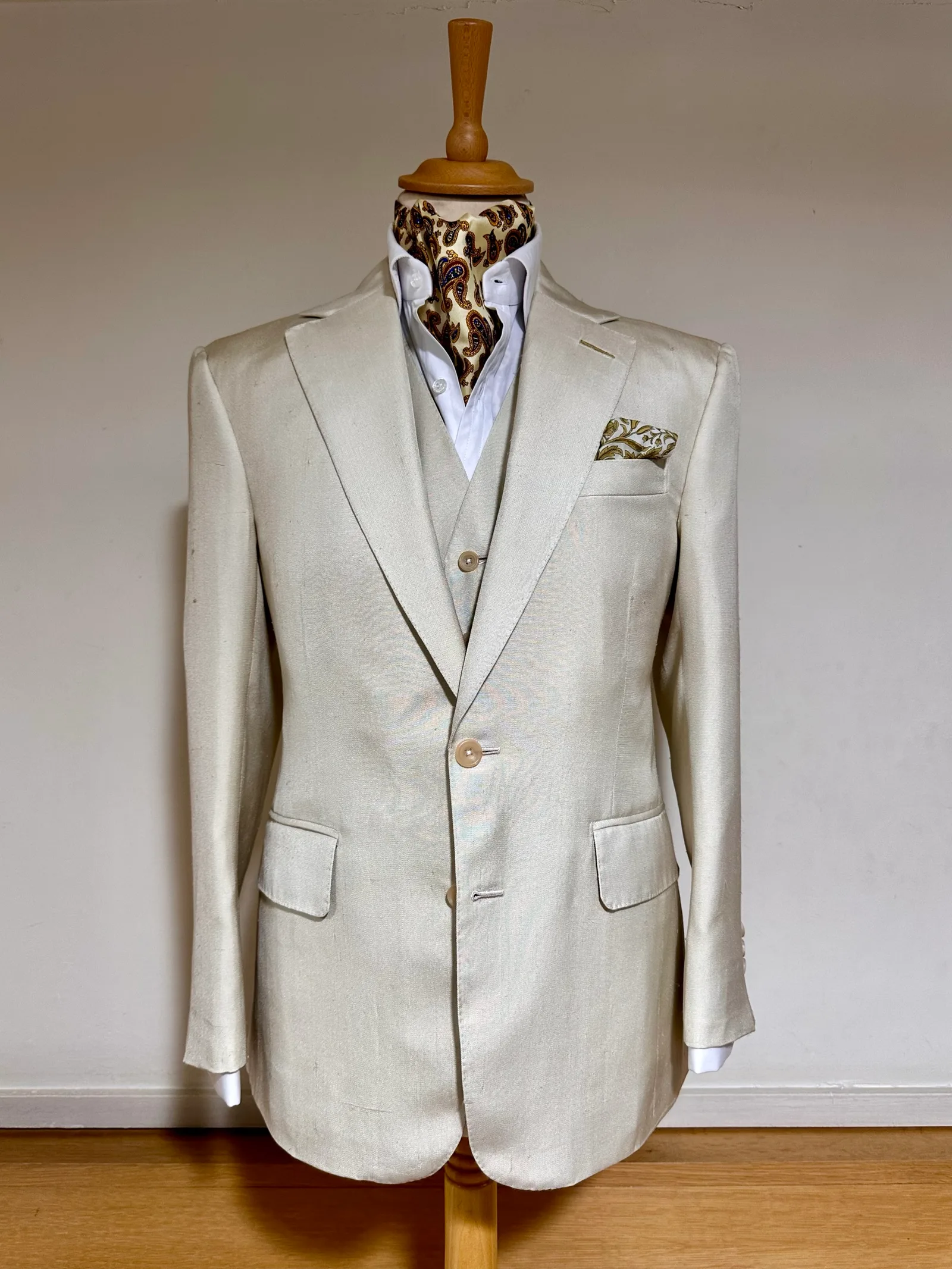 Mannequin view of an ivory summer three-piece suit, with a notch-lapel jacket, pale buttons and a matching six-button waistcoat.