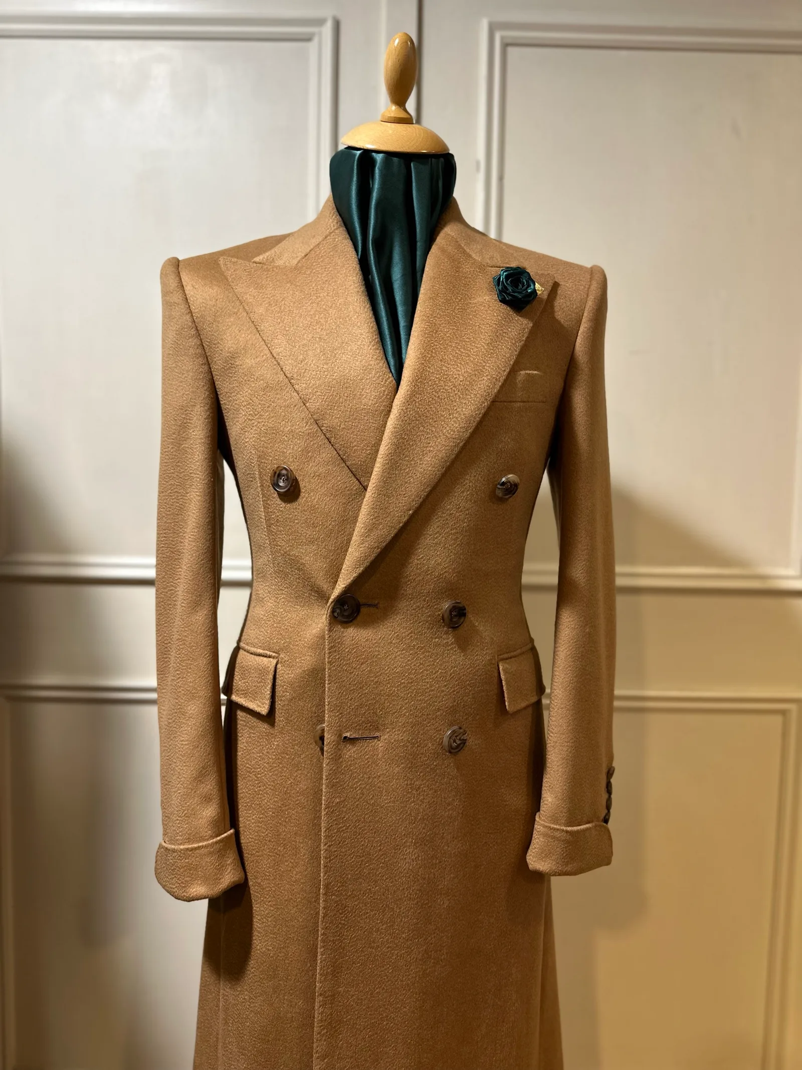 Mannequin view of a camel vicuña double-breasted overcoat, with broad peak lapels, dark horn buttons and elegant turnback cuffs.