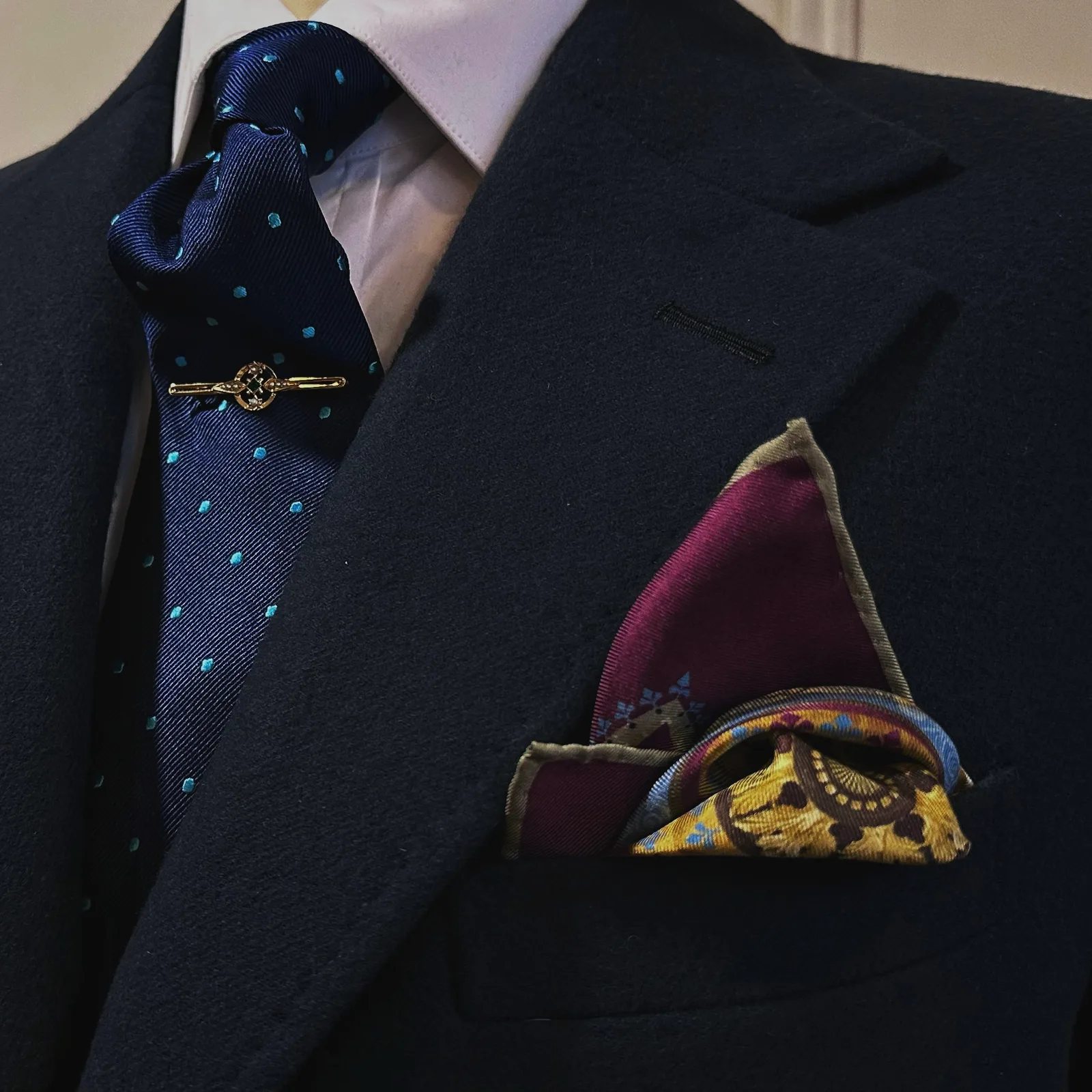 A navy vicuña jacket is styled with dotted silk, a jeweled tie bar and pocket square.