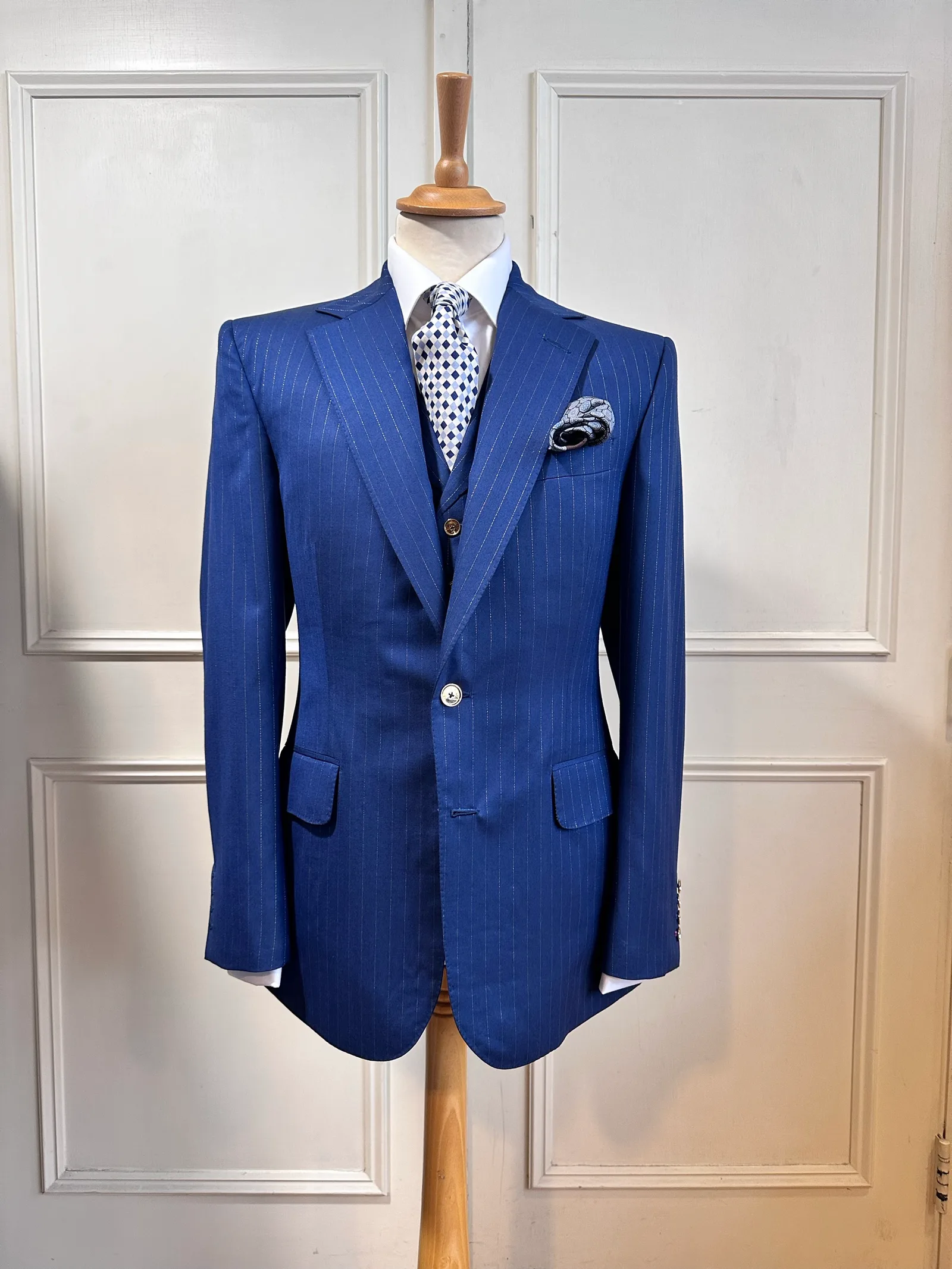 Front mannequin view of the royal blue chalkstripe three-piece suit, tailored with fine pale chalkstripes, notch lapels and decorative gilt buttons.