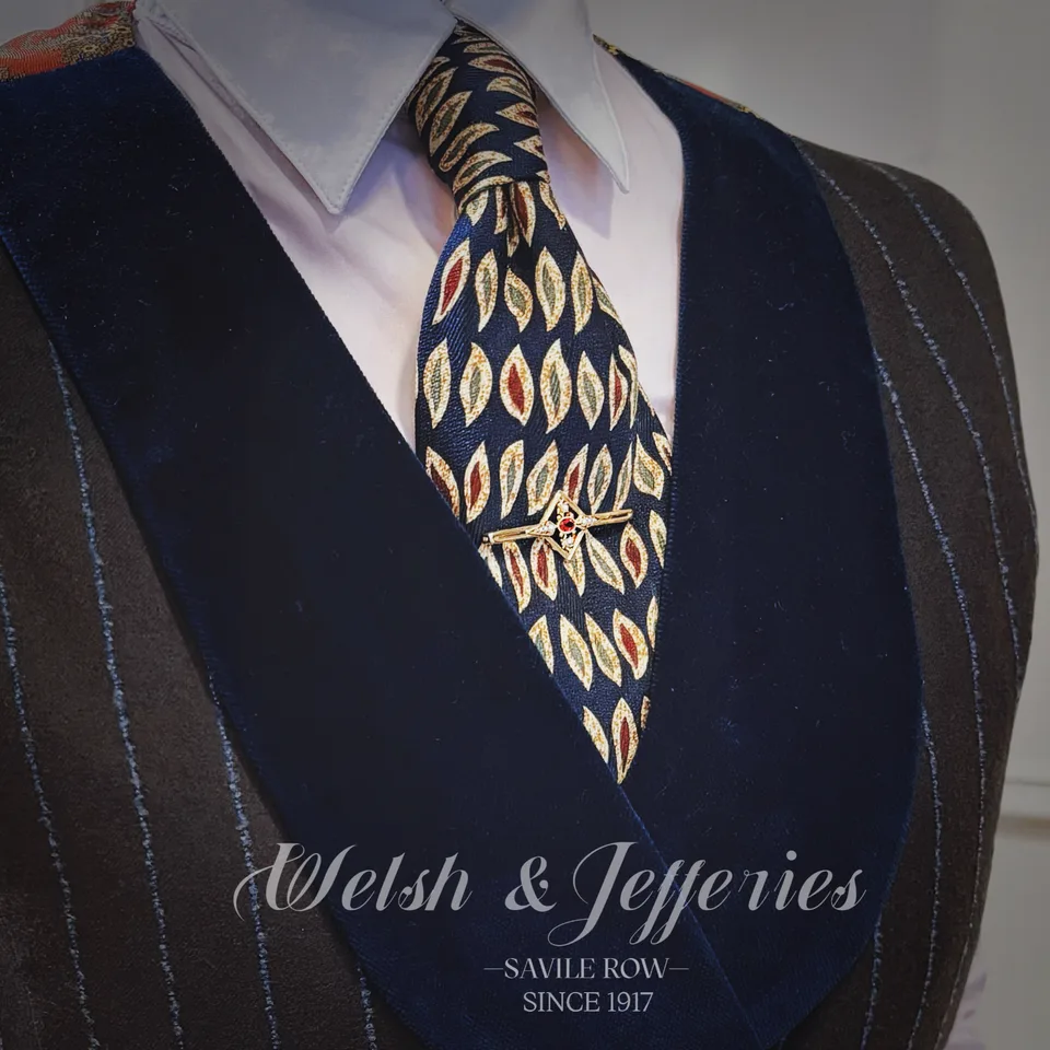 Gold compass-like tie bar centred with a round ruby and bright stone accents against navy leaf-patterned silk.