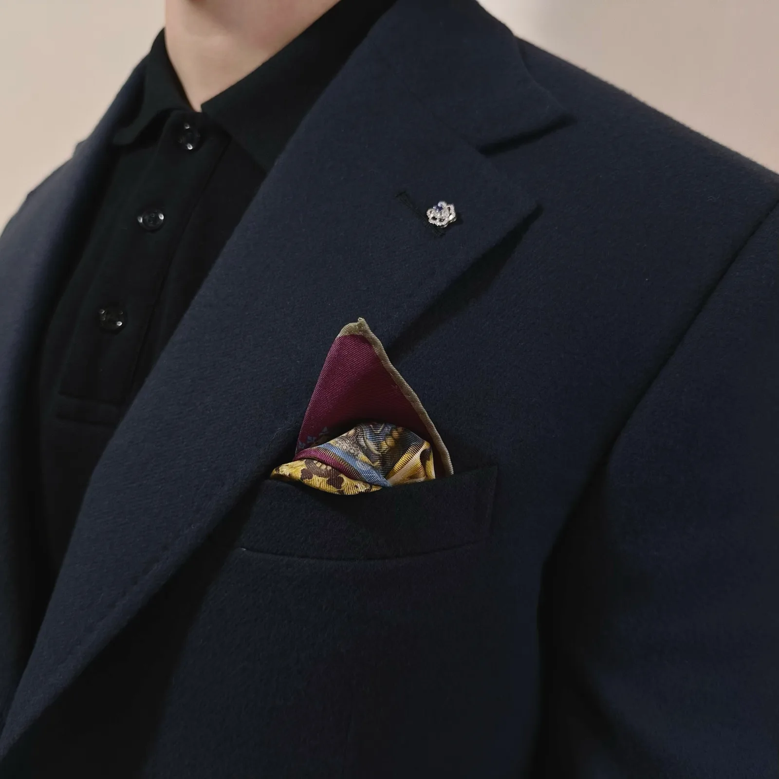 Close view of a navy vicuña lapel, discreet pin and folded patterned pocket square.