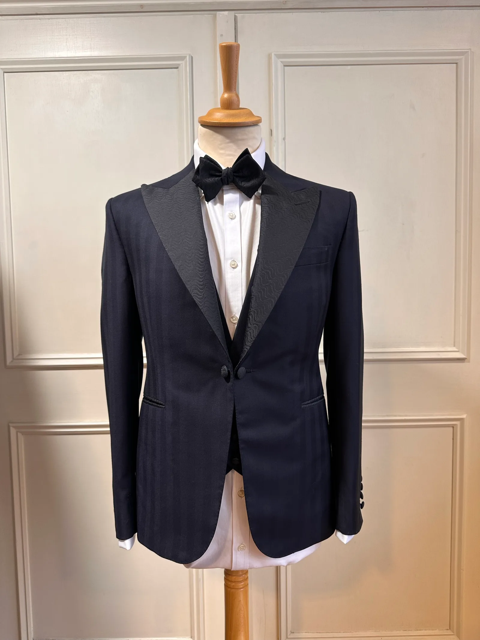 Front mannequin view of the midnight jacquard peak-lapel tuxedo, tailored with textured black peak lapels, a one-button front and midnight-blue cloth.