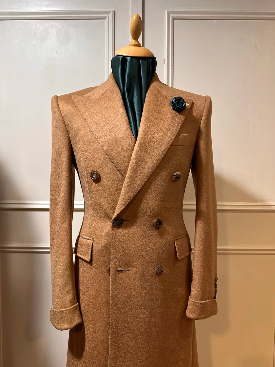 Mannequin view of a camel vicuña double-breasted overcoat, with broad peak lapels, dark horn buttons and elegant turnback cuffs.
