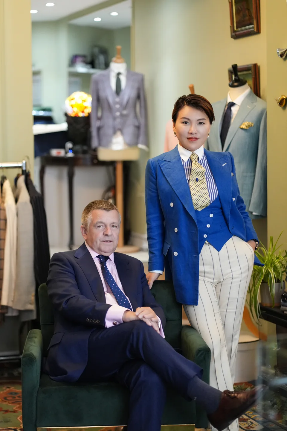 Two tailoring partners pose with relaxed confidence in the garment-filled salon.