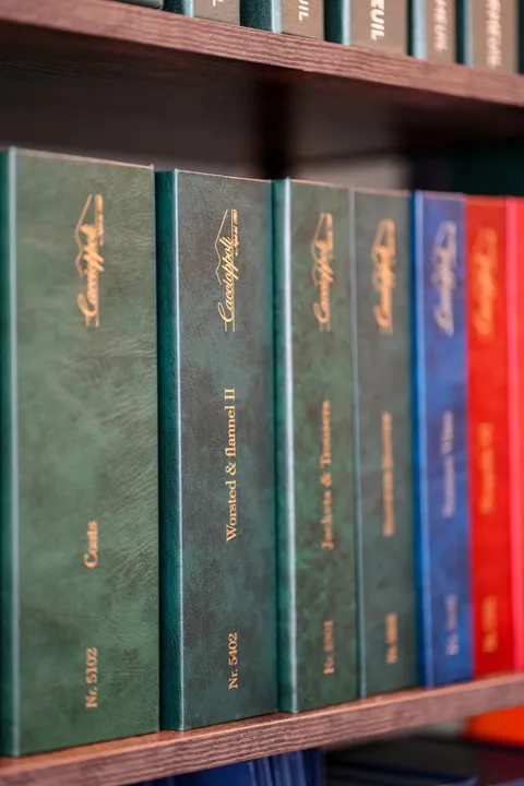 Cloth bunch books — coats, worsteds and flannels — on a dark wood shelf