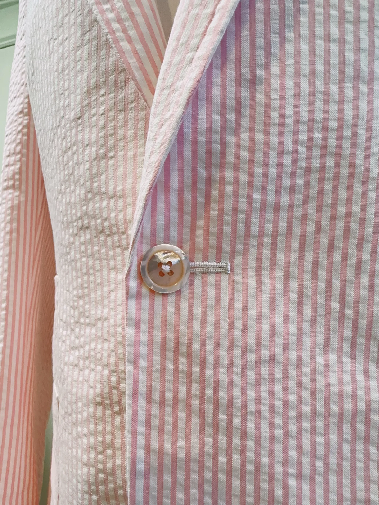 Close view of the pink seersucker jacket’s pale front button and rippled striped texture.