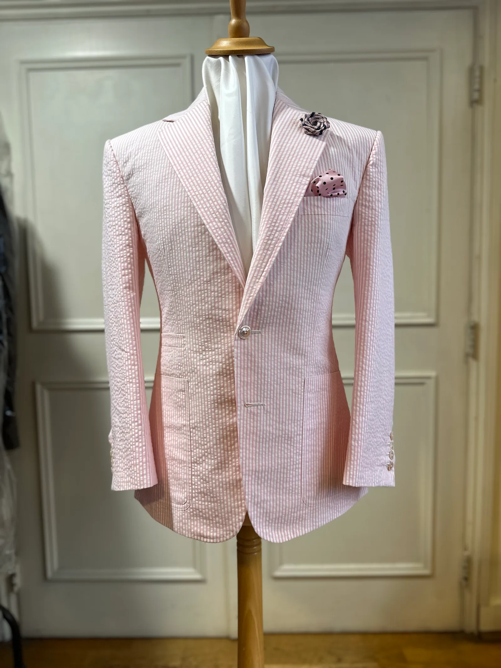 Mannequin view of a pale-pink seersucker jacket, cut with broad peak lapels, a single pale button and rounded fronts.