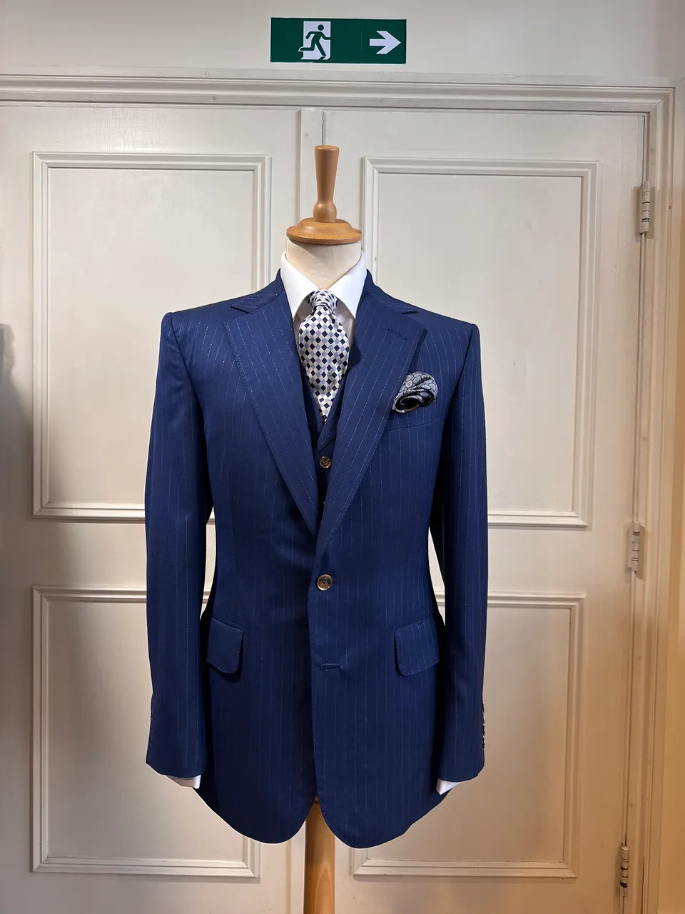 Front mannequin view of the royal blue chalkstripe three-piece suit, tailored with fine pale chalkstripes, notch lapels and decorative gilt buttons.