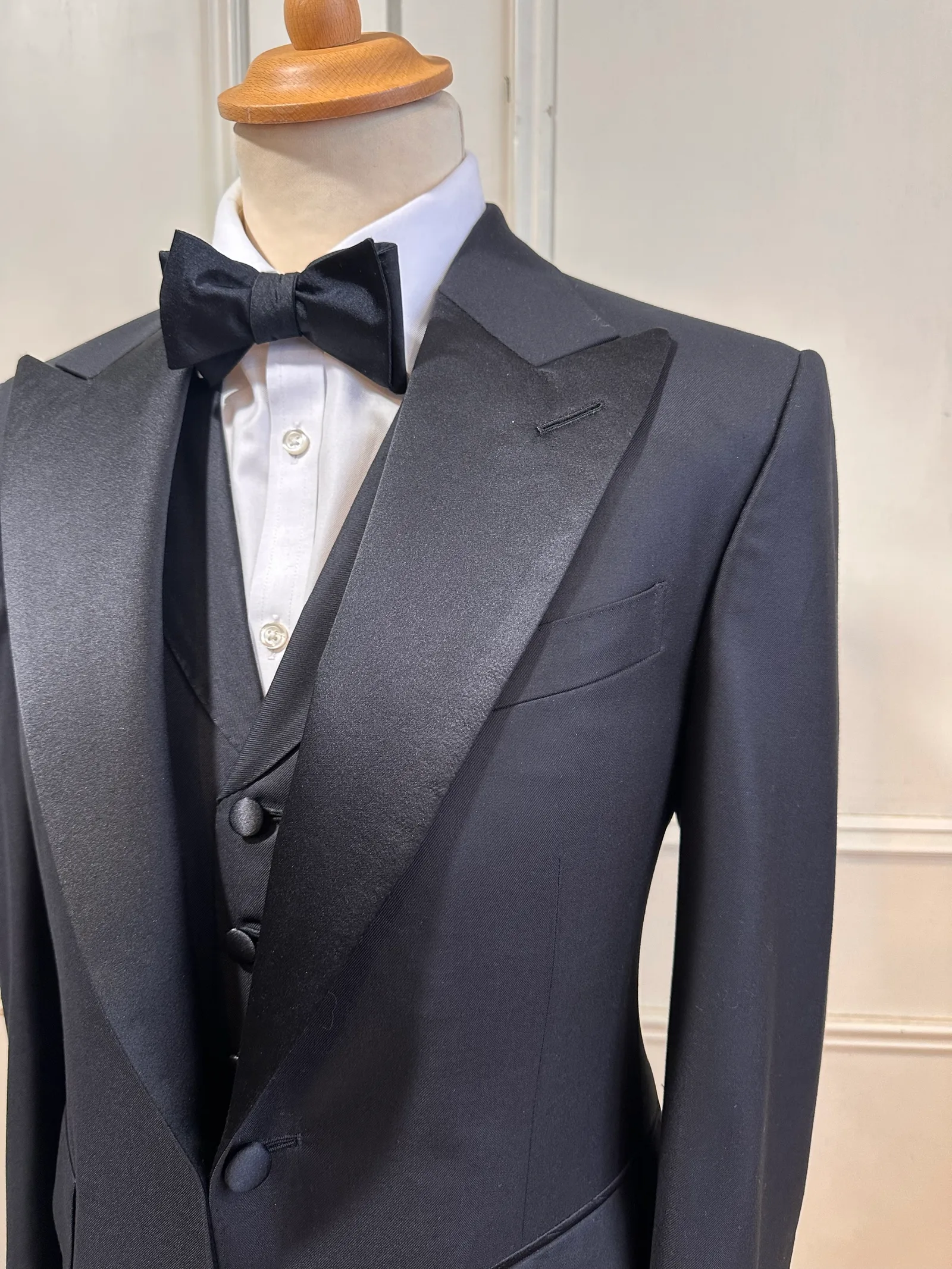Upper-body view of the black satin peak-lapel tuxedo, highlighting broad satin peak lapels, a clean one-button front and covered buttons.