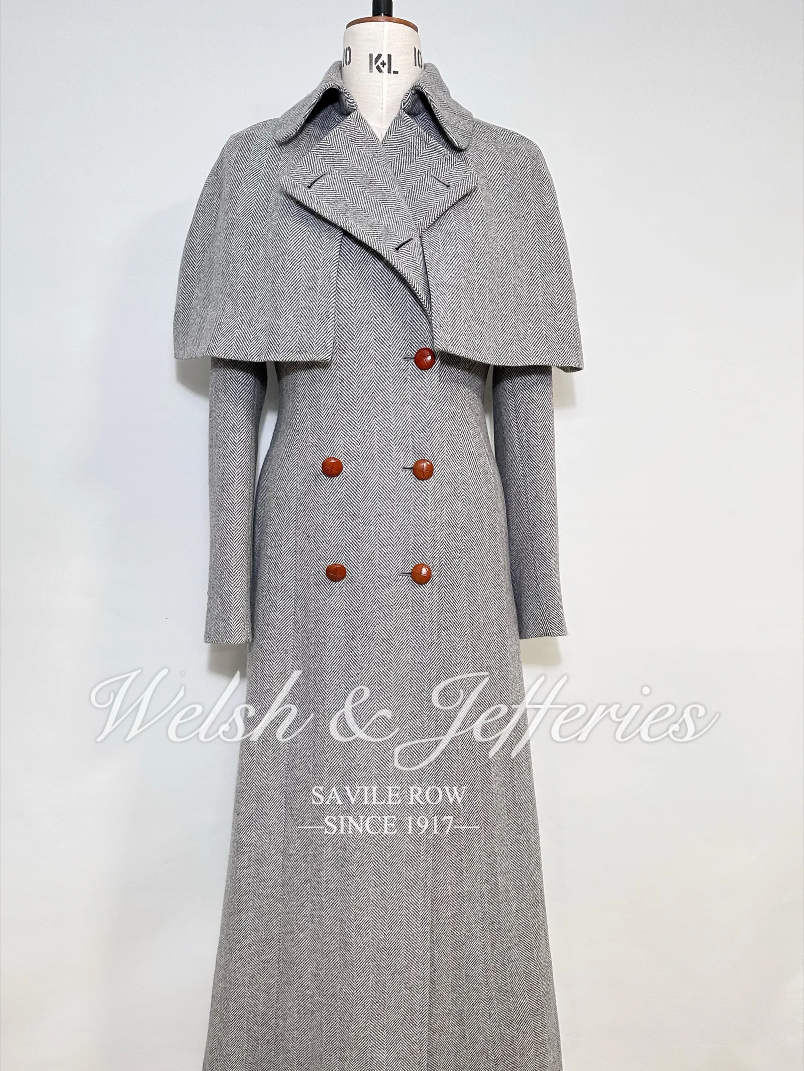 Alternate full view of the pale-grey herringbone cape overcoat.