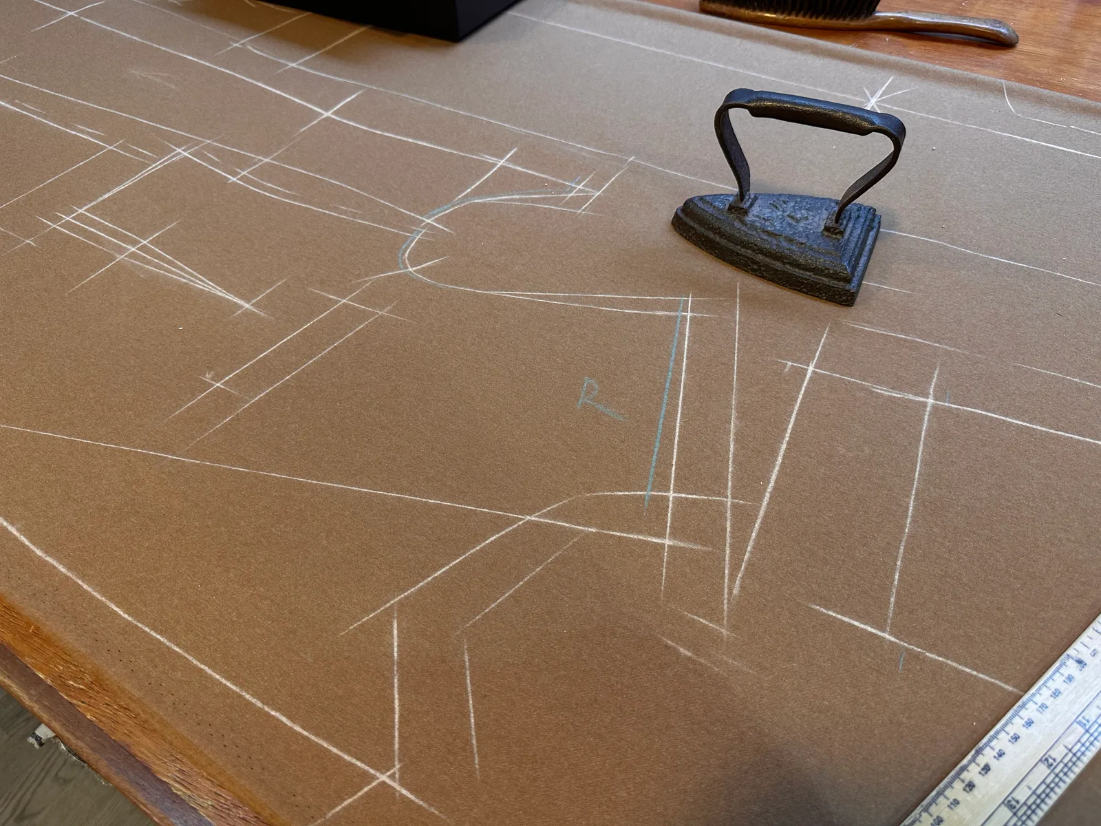 Tailoring pattern lines are chalked across brown cloth beside a traditional iron and ruler.