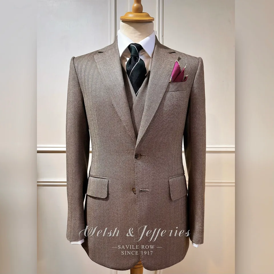 Taupe herringbone three-piece suit with a long clean front and matching waistcoat.