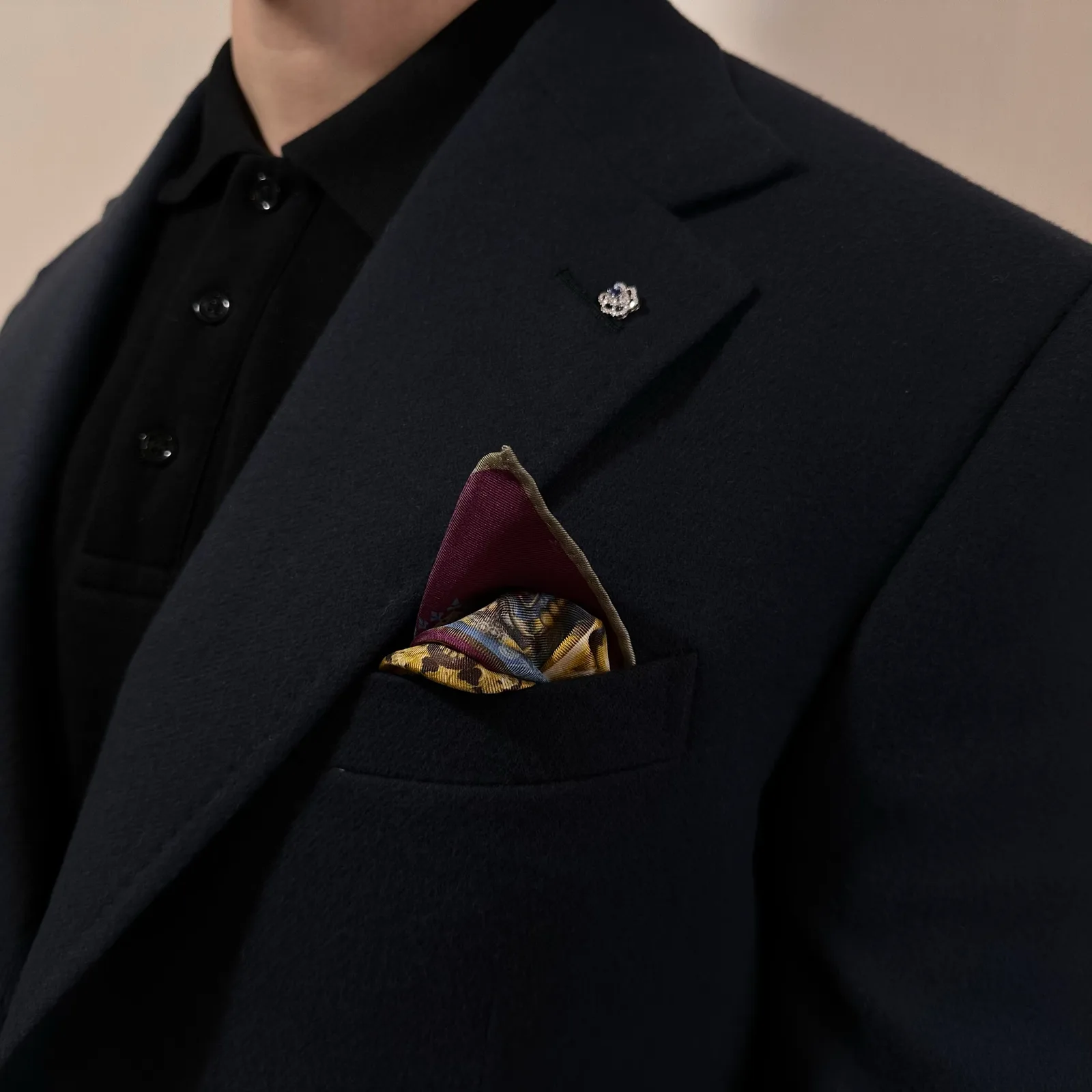 A midnight navy vicuña jacket is styled with a patterned pocket square and lapel pin.