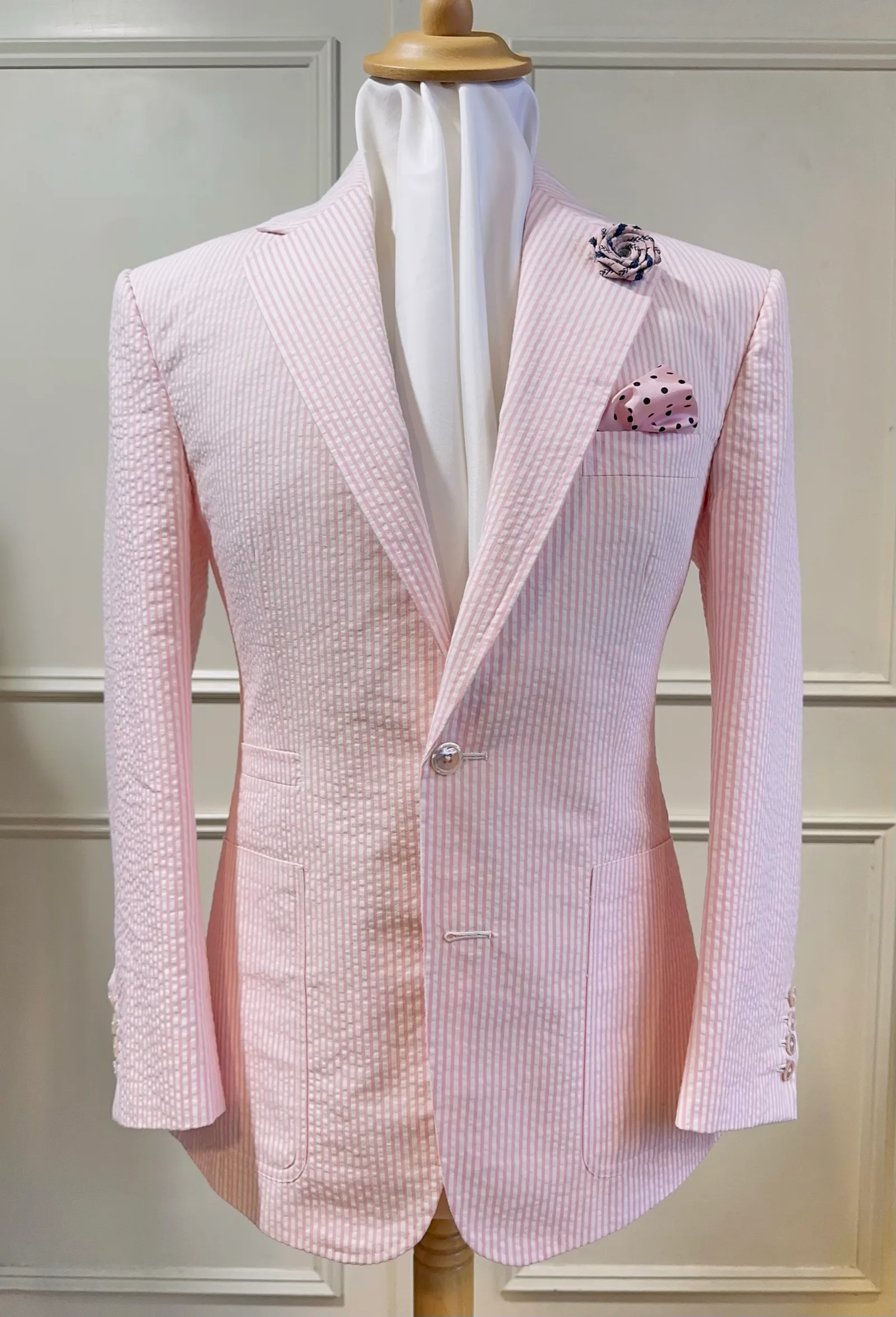 Mannequin view of a pale-pink seersucker jacket, cut with broad peak lapels, a single pale button and rounded fronts.