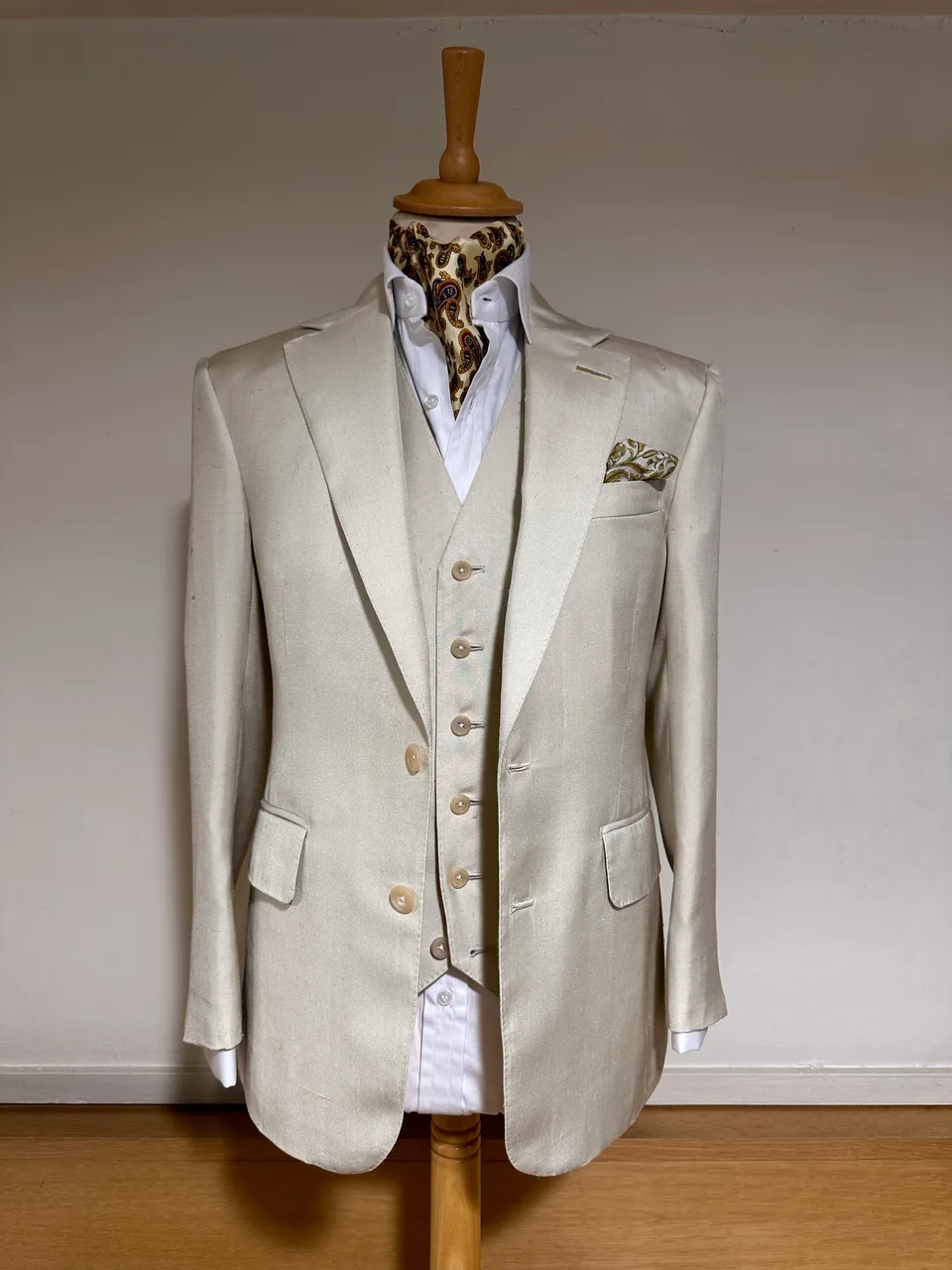 Mannequin view of an ivory summer three-piece suit, with a notch-lapel jacket, pale buttons and a matching six-button waistcoat.