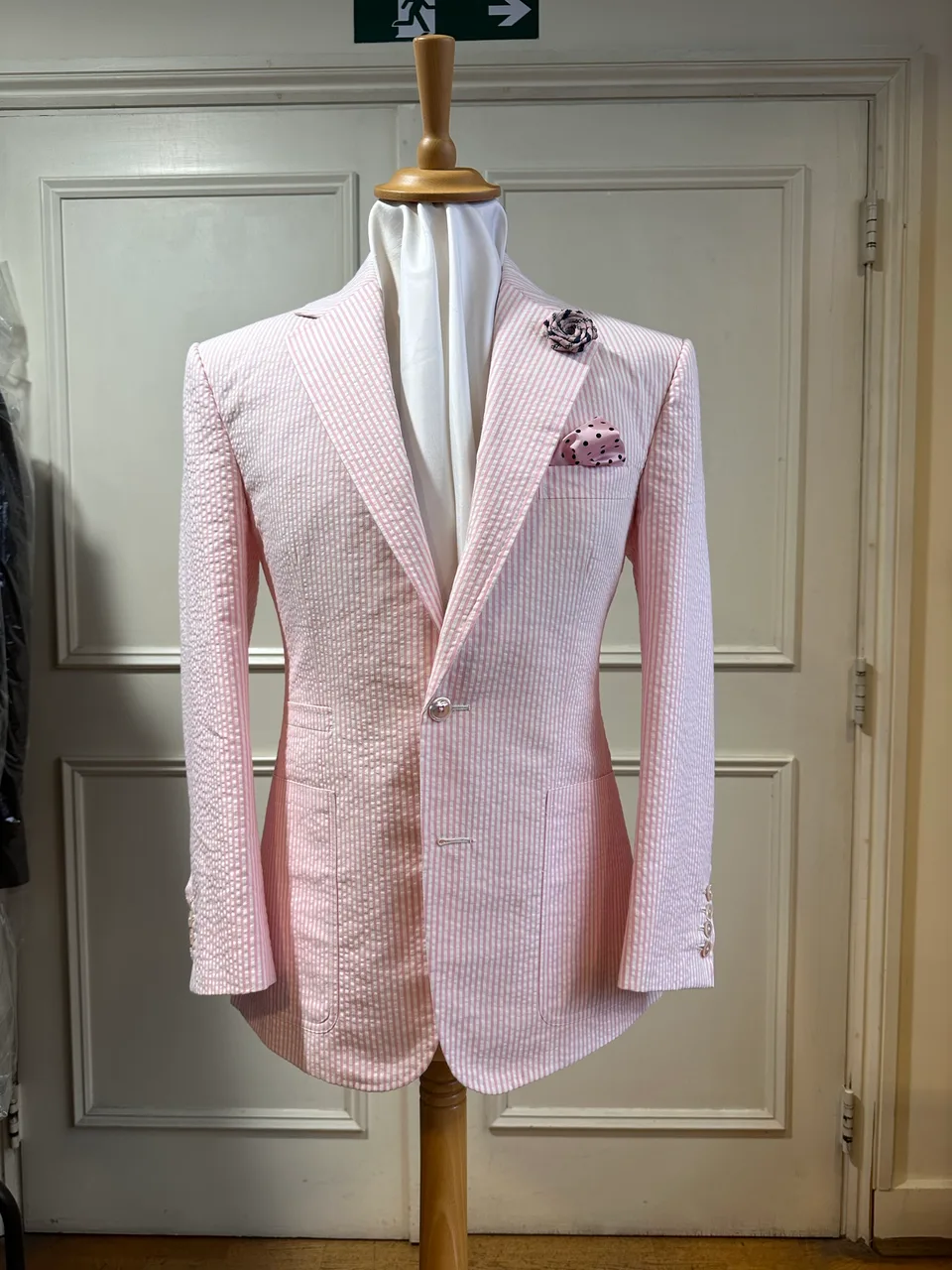 Mannequin view of a pale-pink seersucker jacket, cut with broad peak lapels, a single pale button and rounded fronts.