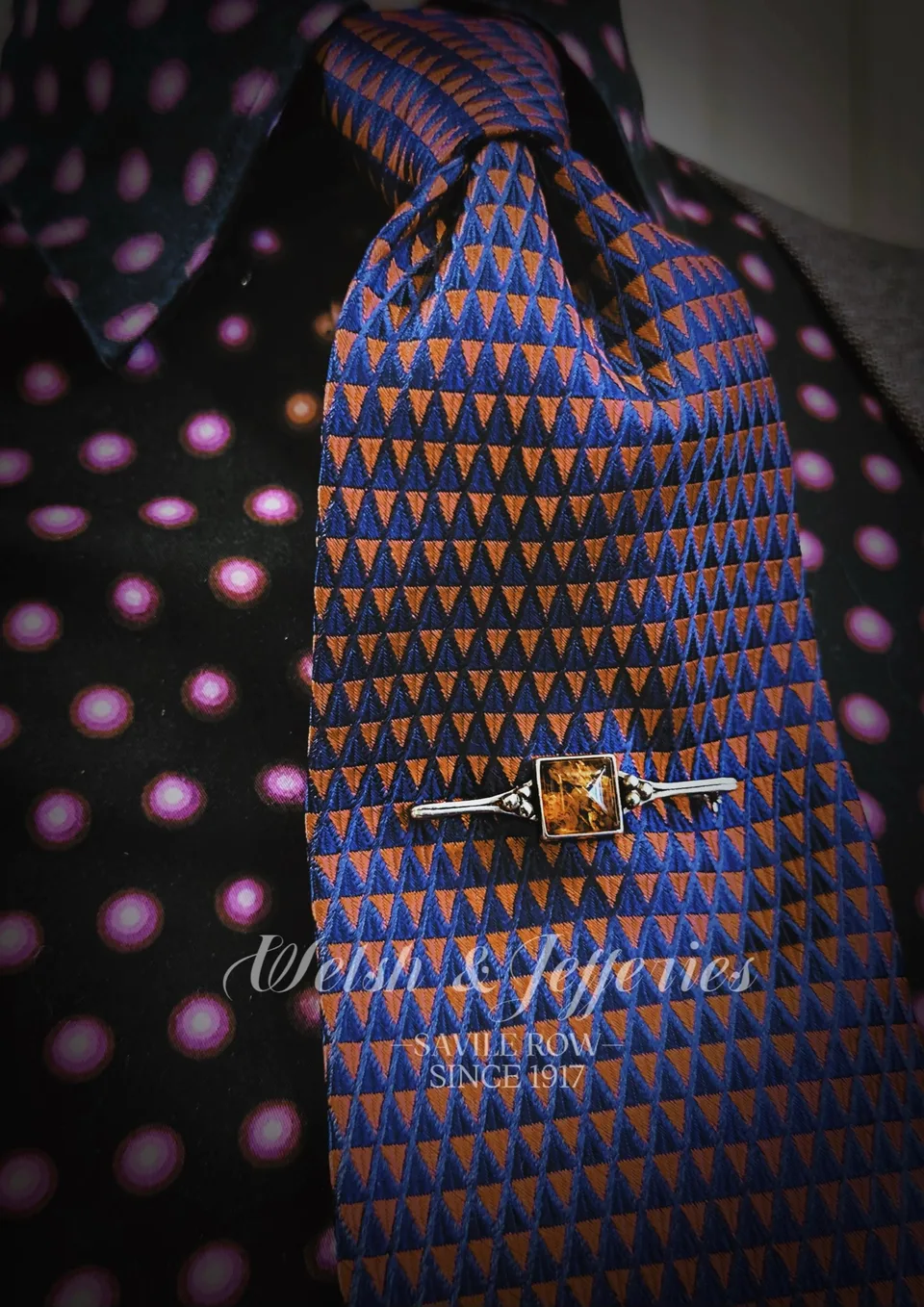 Art Deco tie bar with a square golden citrine and diamond-set white-metal shoulders on patterned blue silk.