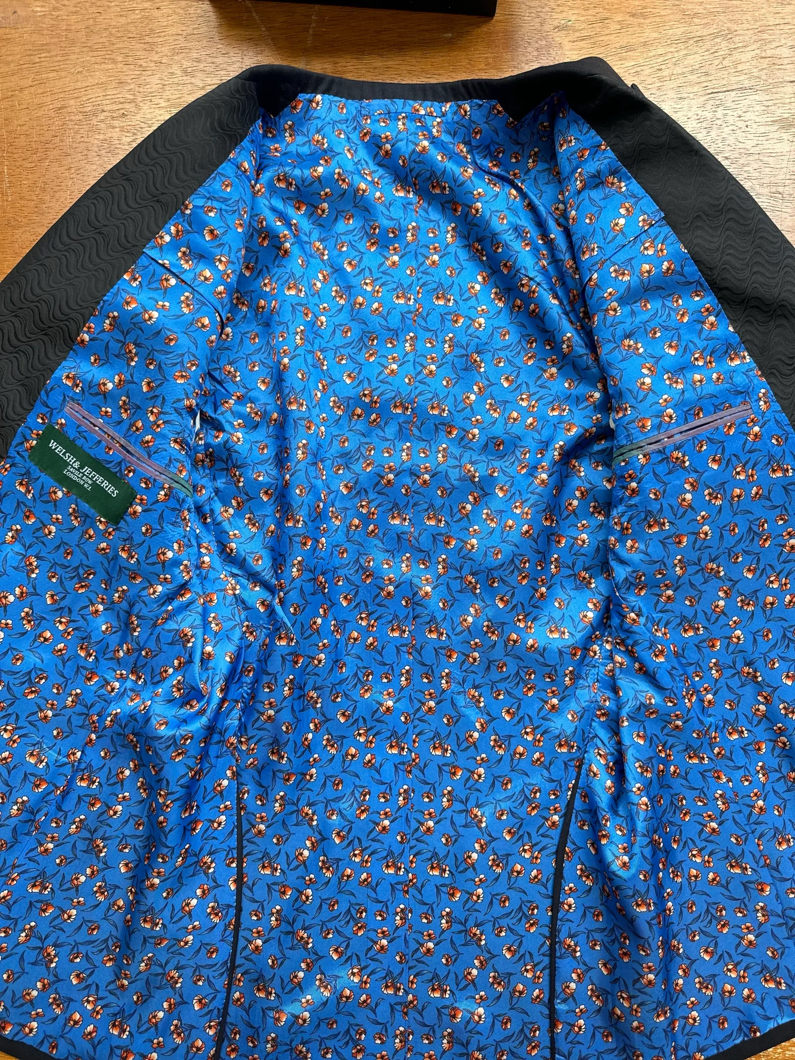 Interior view of the midnight jacquard peak-lapel tuxedo, revealing a vivid cobalt lining scattered with small copper flowers.