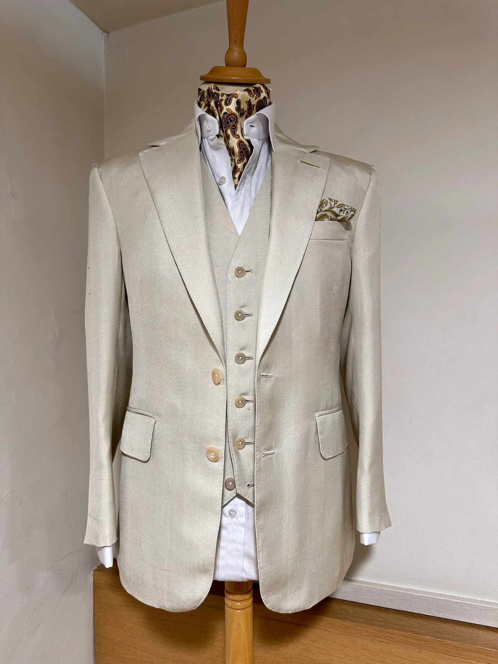 Mannequin view of an ivory summer three-piece suit, with a notch-lapel jacket, pale buttons and a matching six-button waistcoat.
