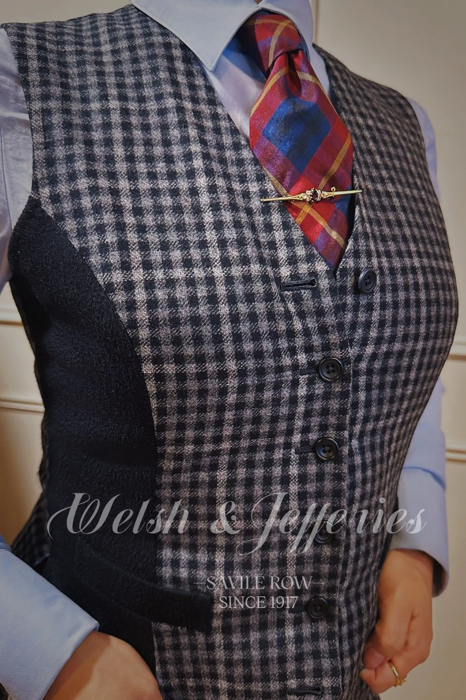 Antique-style gold bar brooch with a deep garnet centre worn across a red checked tie and checked waistcoat.